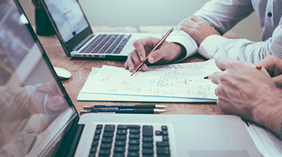 Ivans Exchange Close up of two laptops and two colleagues interacting with stack of papers.